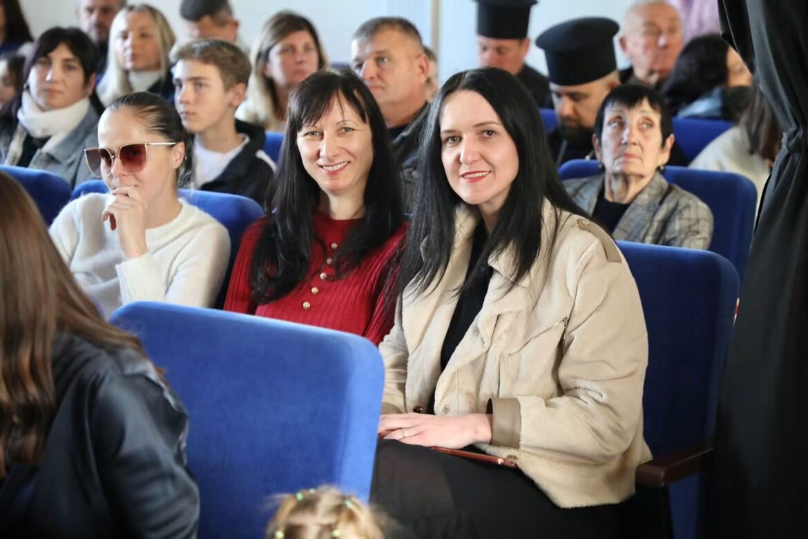 Гості урочистостей сидять у синіх кріслах актової зали, серед них жінки, підлітки і священники в камилавках