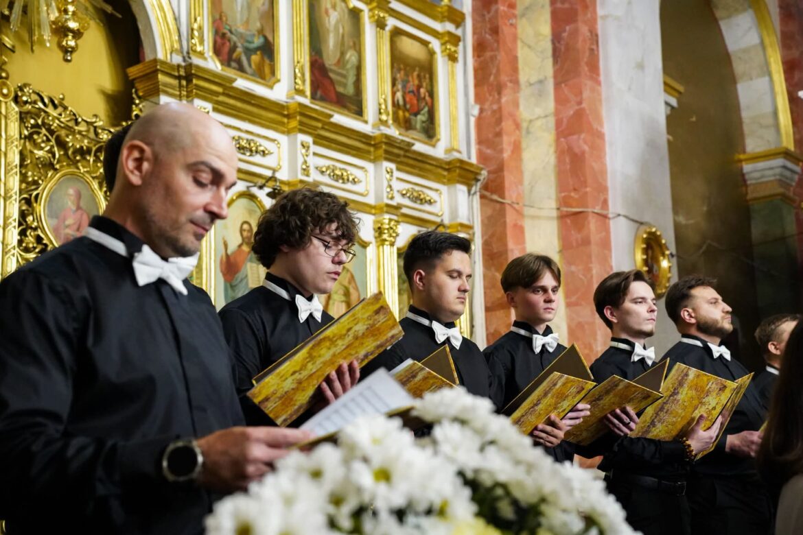 Хористи в чорних сорочках з білими метеликами співають із золотистими папками біля позолоченого іконостаса