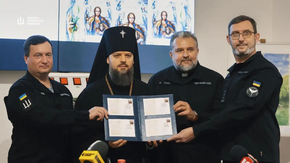 Архієпископ у чорному клобуку, священник із нашивкою «Холодов» і двоє представників ГУР у темній формі тримають розкриту папку з чотирма конвертами з маркою; позаду на екрані образ Архангела, зліва логотип «Головне управління розвідки»