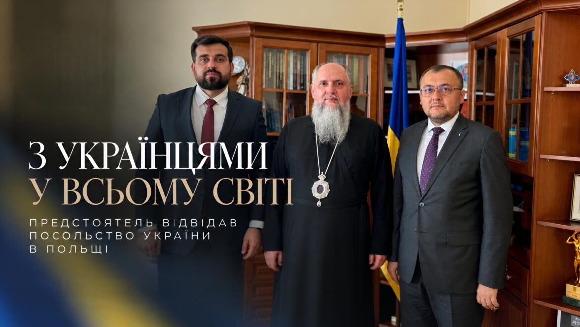 Православний архієрей у чорному підряснику з панагією і двоє чоловіків у темних костюмах стоять у кабінеті з книжковими шафами біля державного прапора України; напис «Митрополит Епіфаній відвідав Посольство України в Польщі. Церква там, де її люди. Навіть далеко від дому»